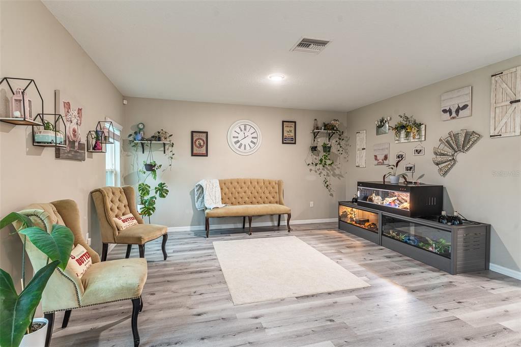 A living room features light wood-look flooring, a tufted bench, two armchairs, and reptile enclosures — 5508 ARLINGTON RIVER DRIVE, LAKELAND, FL