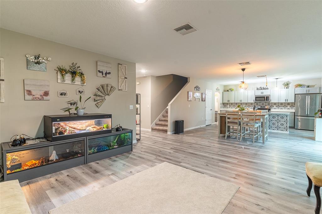 An open-concept living room features wood-look flooring, a large reptile enclosure, and a kitchen beyond — 5508 ARLINGTON RIVER DRIVE, LAKELAND, FL
