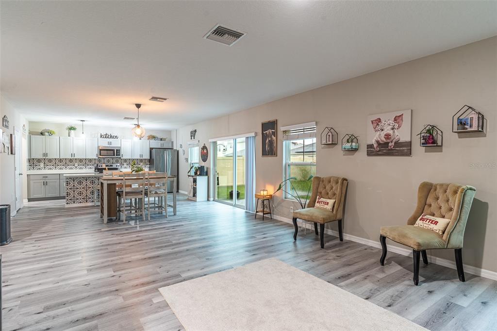 An open-concept living area features light wood-look flooring, a kitchen with gray cabinets, and two tufted chairs — 5508 ARLINGTON RIVER DRIVE, LAKELAND, FL