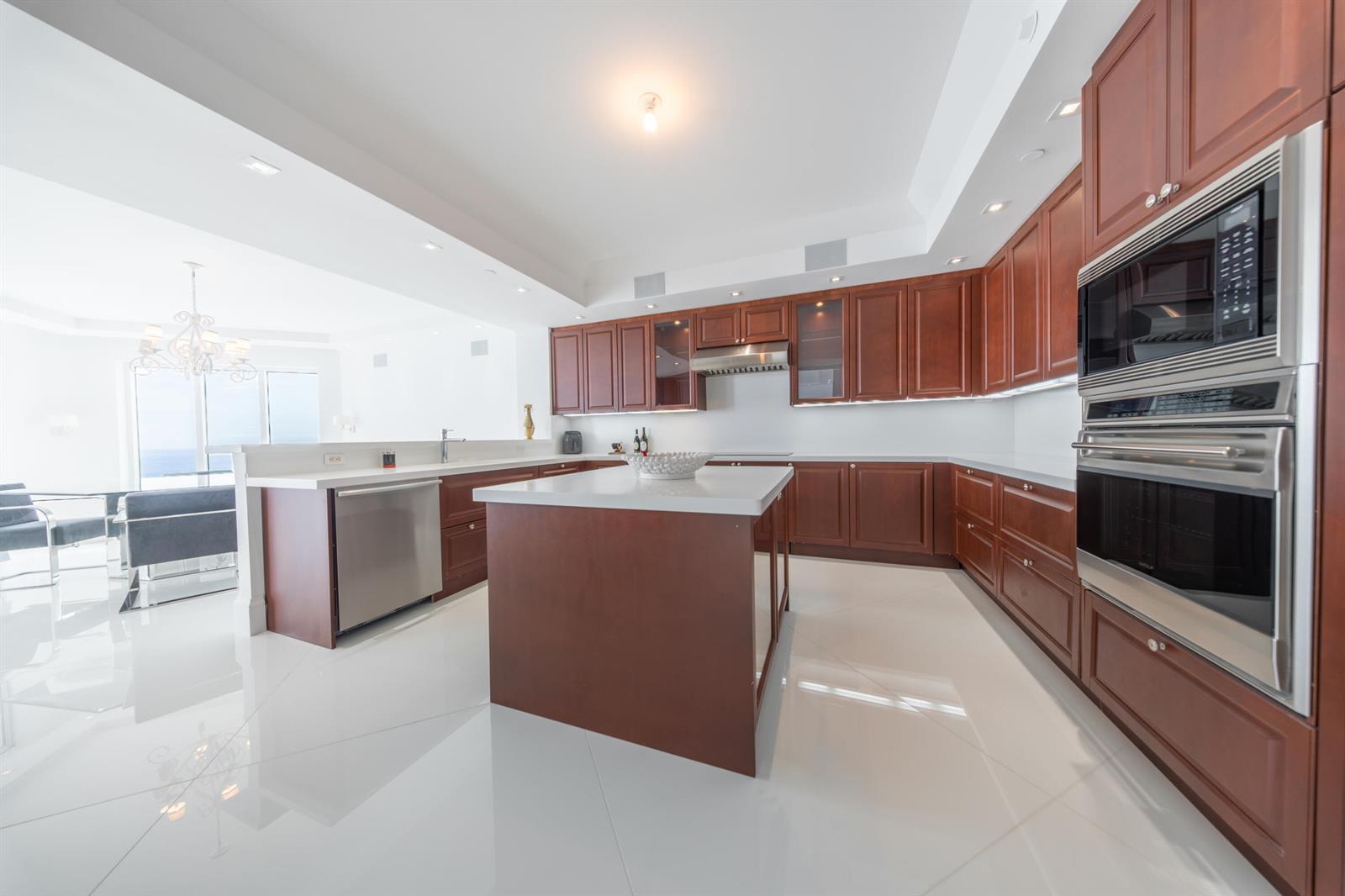A modern kitchen features cherry wood cabinets, white countertops, stainless steel appliances, and tile flooring — 2700 N Ocean Drive # 2501a, Riviera Beach FL 33404, RIVIERA BEACH, FL