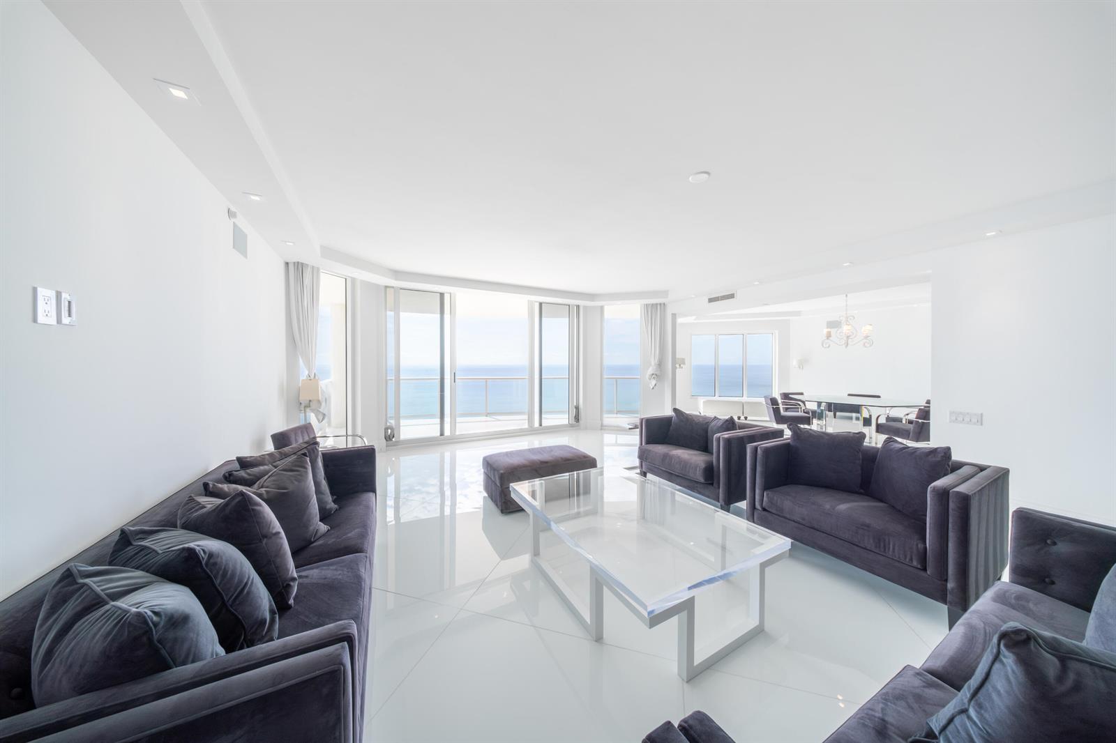 A bright living room features dark gray sofas, a glass coffee table, and ocean views — 2700 N Ocean Drive # 2501a, Riviera Beach FL 33404, RIVIERA BEACH, FL