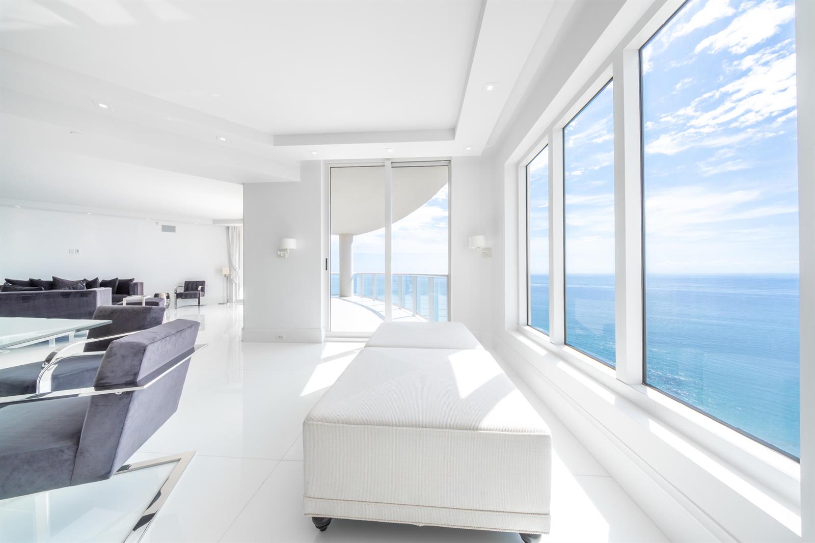 A bright living room features white tile floors, modern furniture, and floor-to-ceiling windows overlooking the ocean — 2700 N Ocean Drive # 2501a, Riviera Beach FL 33404, RIVIERA BEACH, FL