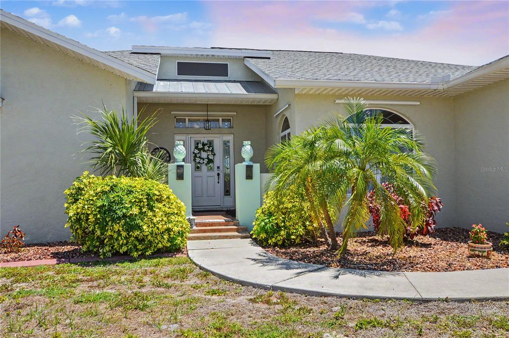 A light-colored house exterior features a front entrance with a walkway and palm trees — 4234 ROCK CREEK DRIVE, PORT CHARLOTTE, FL