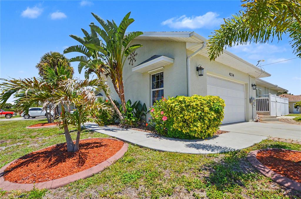 A single-story house with a white garage door, a concrete walkway, and tropical landscaping — 4234 ROCK CREEK DRIVE, PORT CHARLOTTE, FL