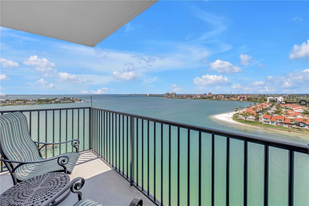 A balcony with a chair and table overlooks a bay with buildings and a beach — 5220 BRITTANY DRIVE S UNIT 1202, ST PETERSBURG, FL
