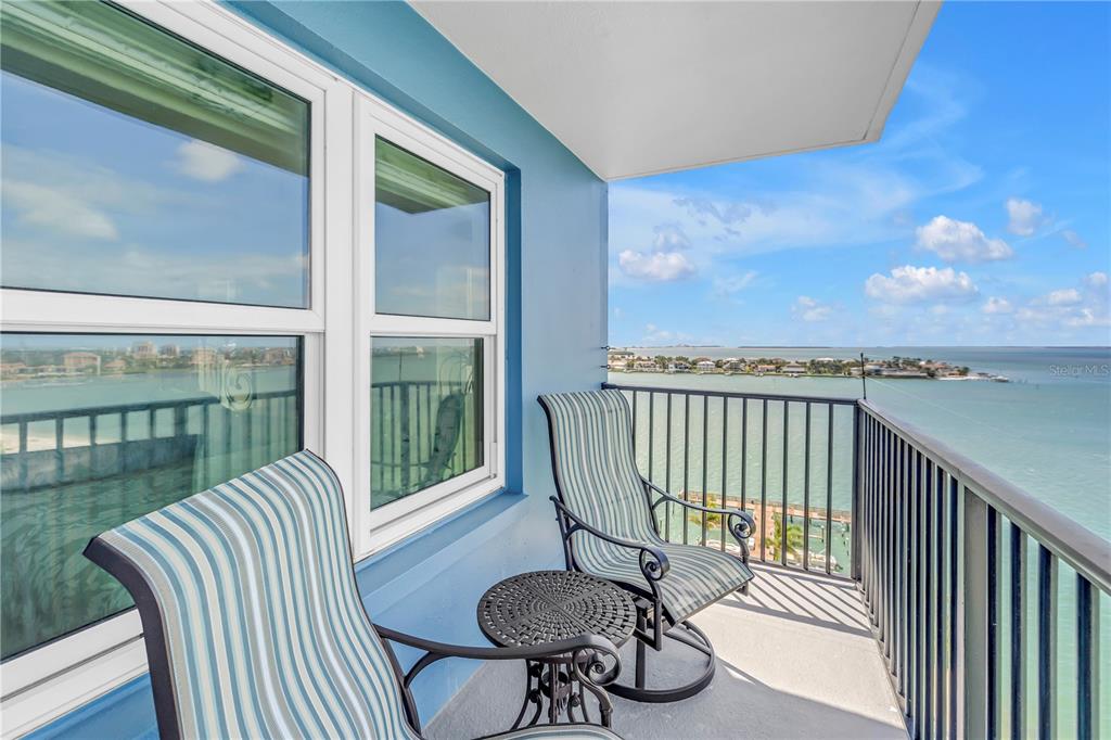 A balcony with two chairs and a small table overlooks a bay and coastline — 5220 BRITTANY DRIVE S UNIT 1202, ST PETERSBURG, FL