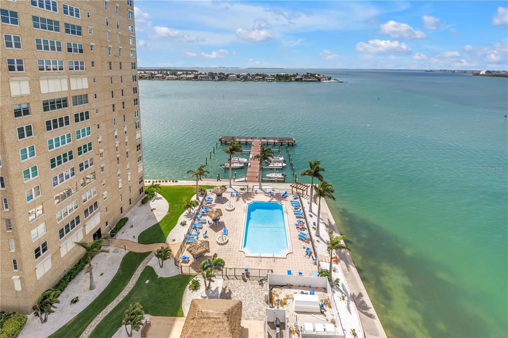 An aerial view shows a high-rise building beside a swimming pool and a boat dock — 5220 BRITTANY DRIVE S UNIT 1202, ST PETERSBURG, FL