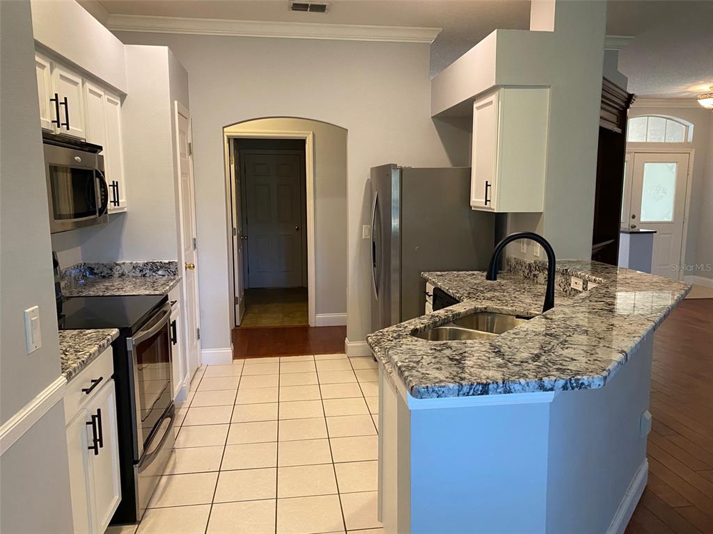 A kitchen features white cabinets, granite countertops, stainless steel appliances, and tile flooring — 460 PICKFAIR TERRACE, LAKE MARY, FL