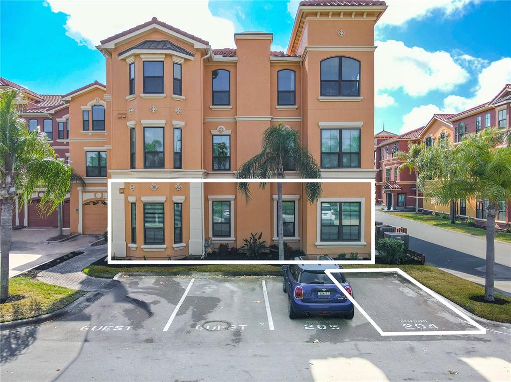 An exterior view of a multi-story stucco building with designated parking spaces in front — 2749 VIA CIPRIANI UNIT 1010B, CLEARWATER, FL
