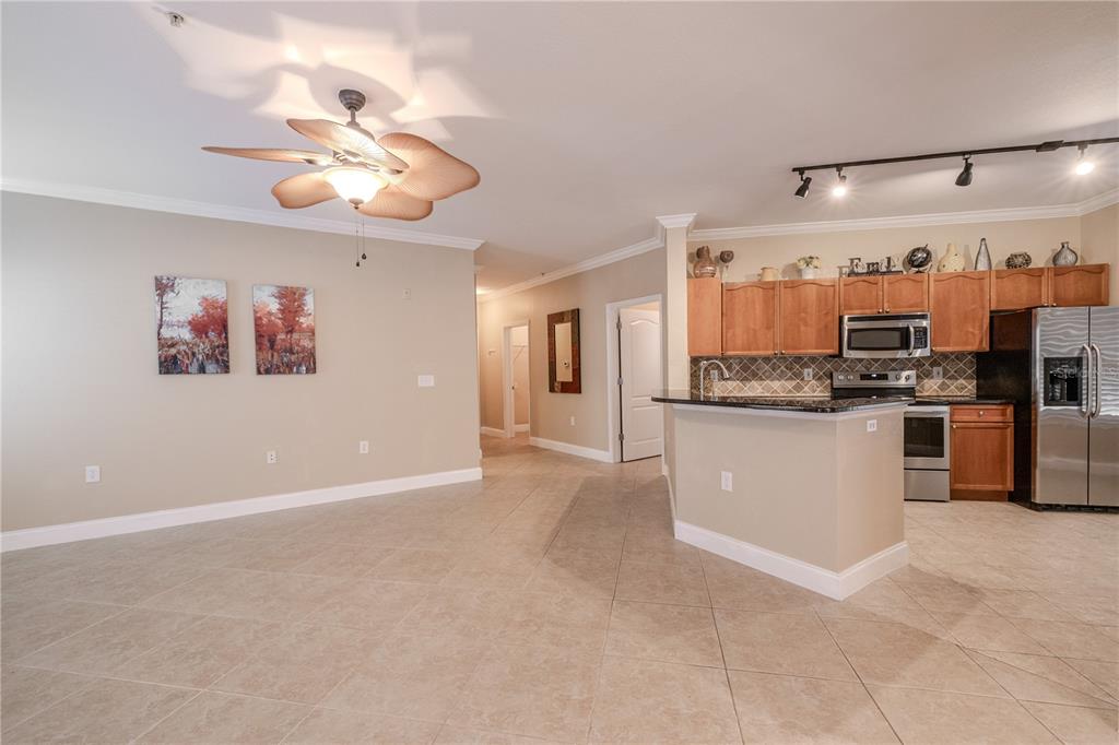 An open-concept kitchen and living area feature tile flooring, wood cabinets, and a ceiling fan — 2749 VIA CIPRIANI UNIT 1010B, CLEARWATER, FL