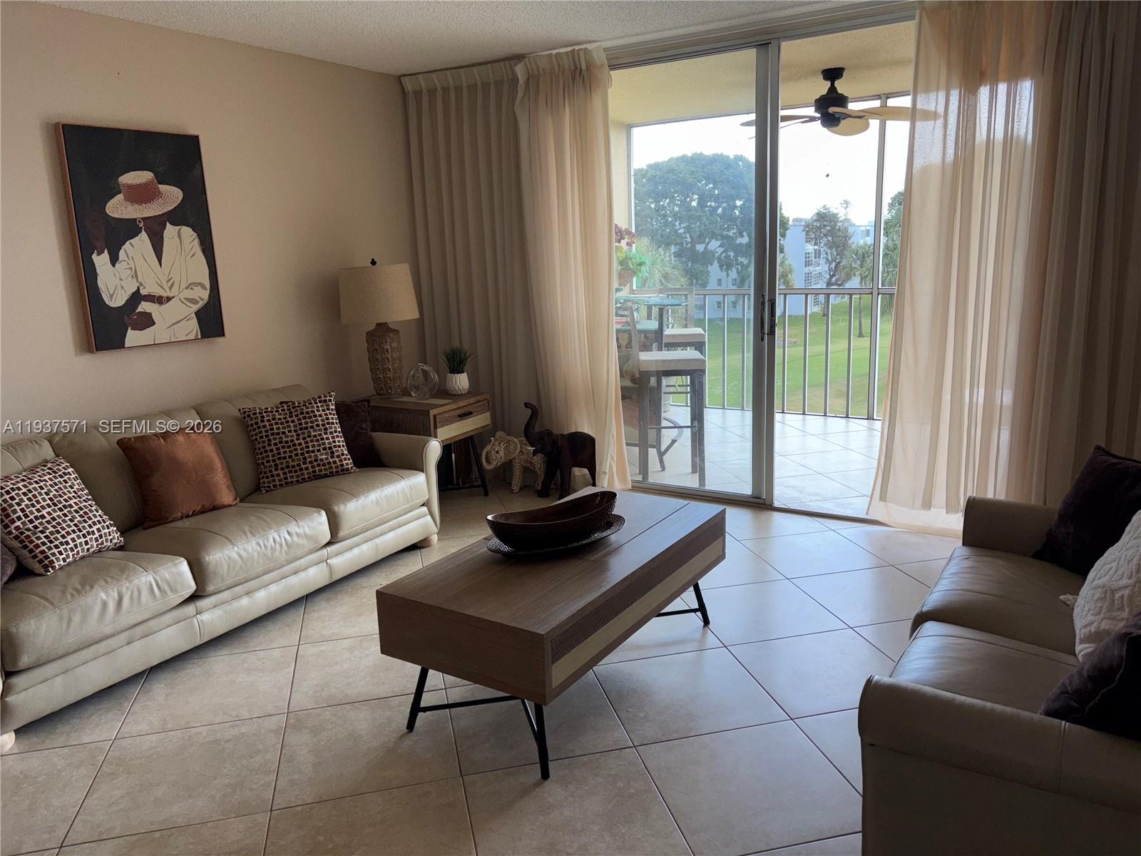 A living room features light-colored leather sofas, a wooden coffee table, and a balcony view — 7690 NW 18th St # 408, Margate FL 33063, MARGATE, FL