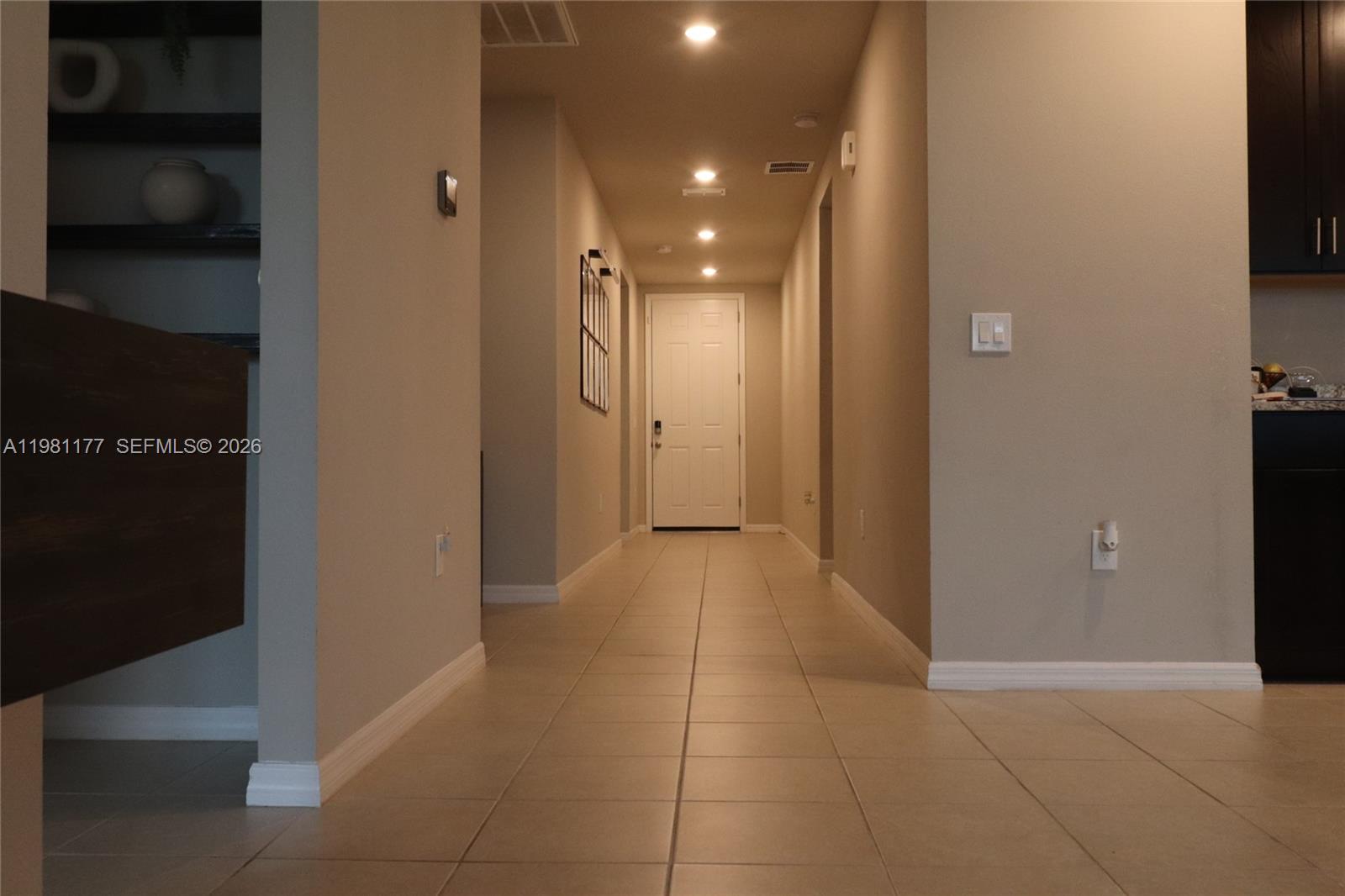 A tiled hallway leads to a white door under recessed lighting in a neutral-toned home — 920 CAMBRIDGE DR, Winter Haven FL 33881, WINTER HAVEN, FL