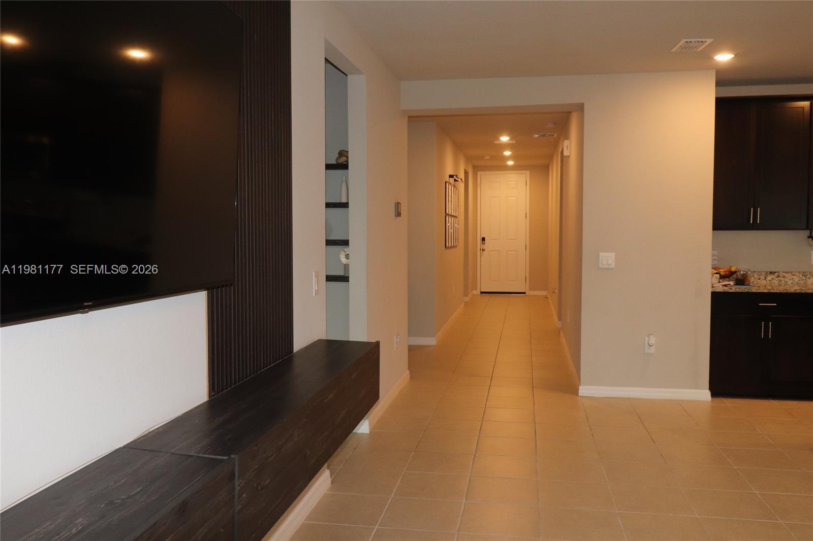 A hallway with tile flooring leads to a front door near a dark kitchen area — 920 CAMBRIDGE DR, Winter Haven FL 33881, WINTER HAVEN, FL