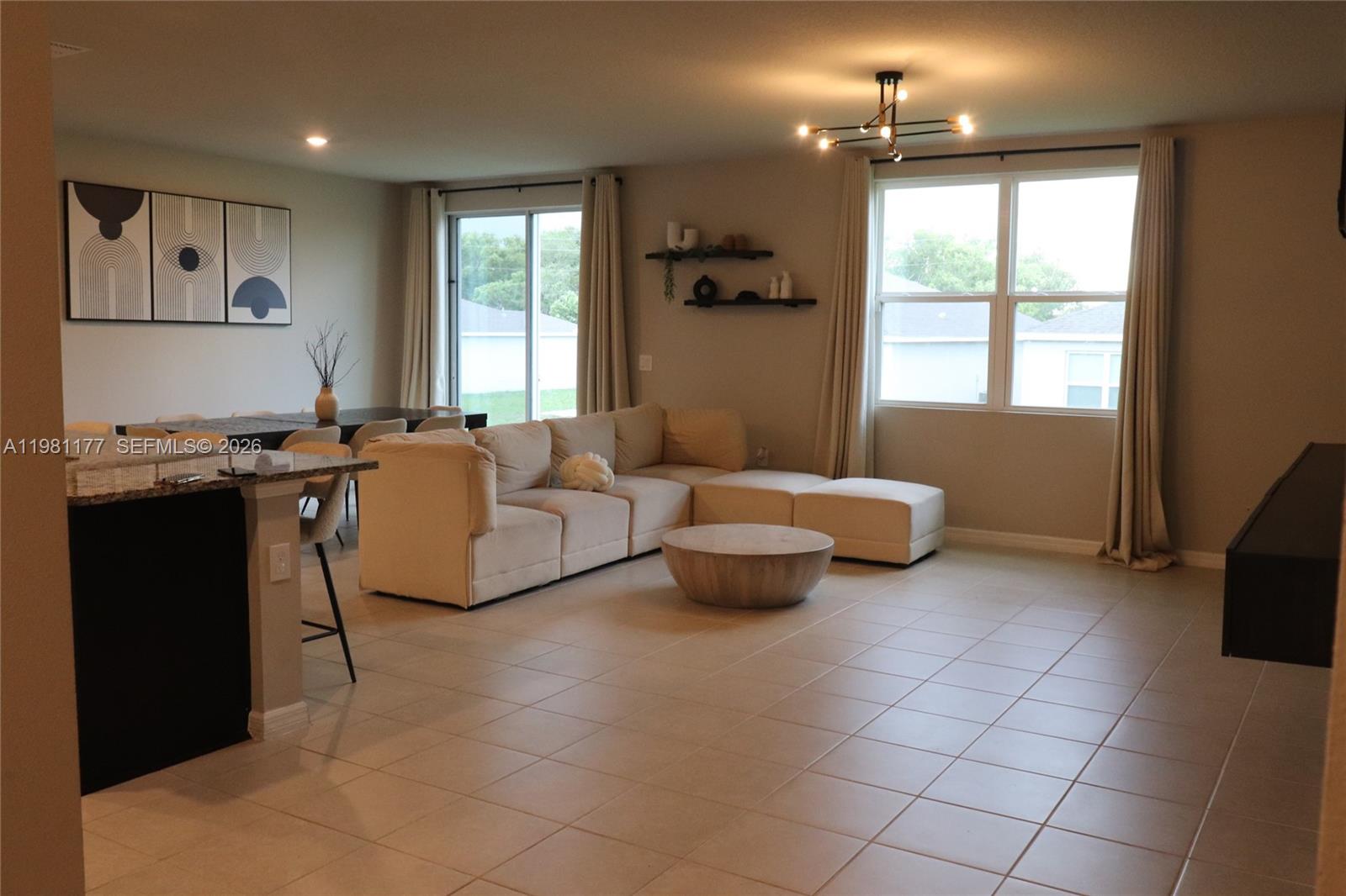 An open-concept living and dining area features tile flooring, a beige sectional, and large windows — 920 CAMBRIDGE DR, Winter Haven FL 33881, WINTER HAVEN, FL