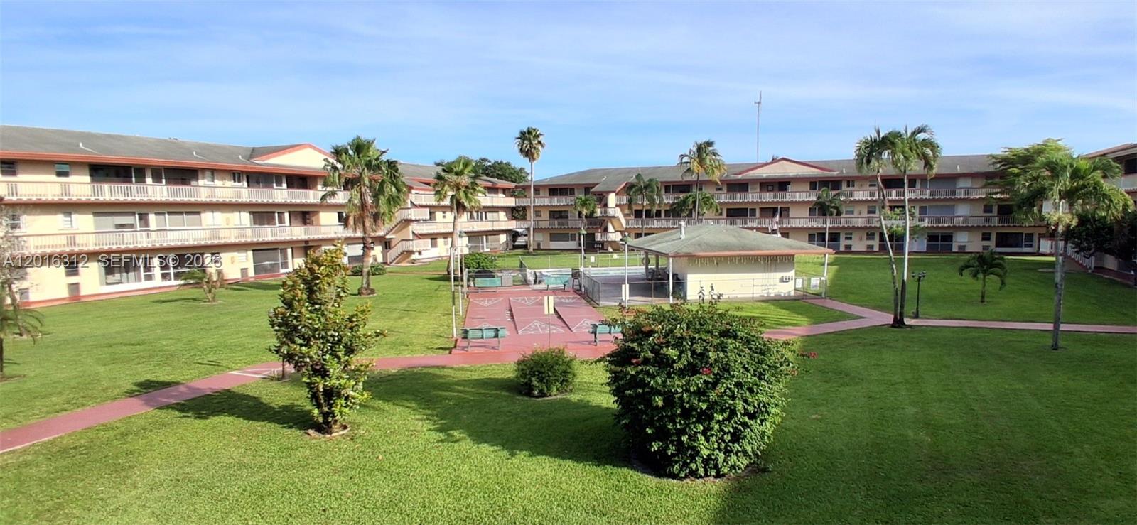 A courtyard view of a multi-story apartment complex featuring a pool, shuffleboard, and landscaping — 5300 Washington St # C212, Hollywood FL 33021, HOLLYWOOD, FL