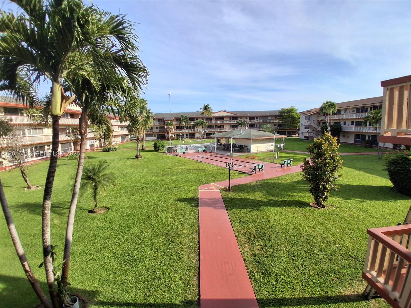 An elevated view of a grassy courtyard with a walkway, shuffleboard courts, and apartment buildings — 5300 Washington St # C212, Hollywood FL 33021, HOLLYWOOD, FL