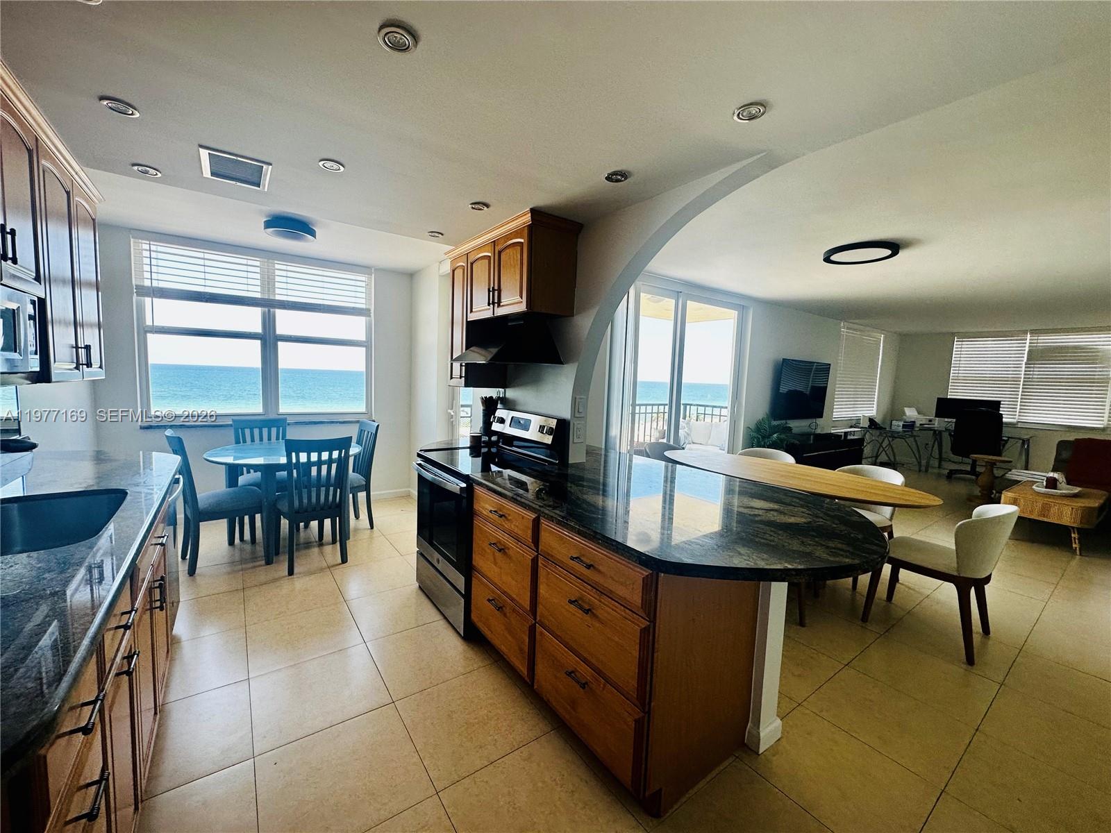 A kitchen with wooden cabinets and a dark countertop overlooks the ocean through windows — 1501 S Ocean Dr # 1006, Hollywood FL 33019, HOLLYWOOD, FL