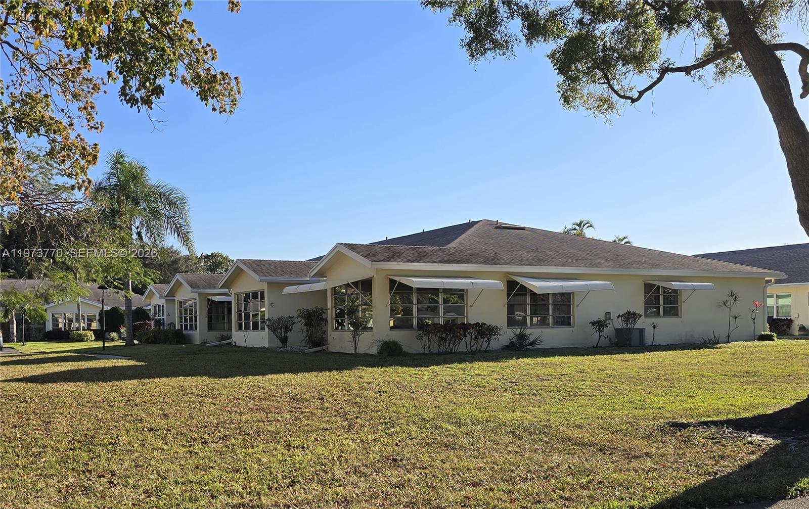 A low-rise, light-colored residential building with multiple windows and awnings sits on a grassy lawn — 5162 Lakefront Blvd # D, Delray Beach FL 33484, DELRAY BEACH, FL