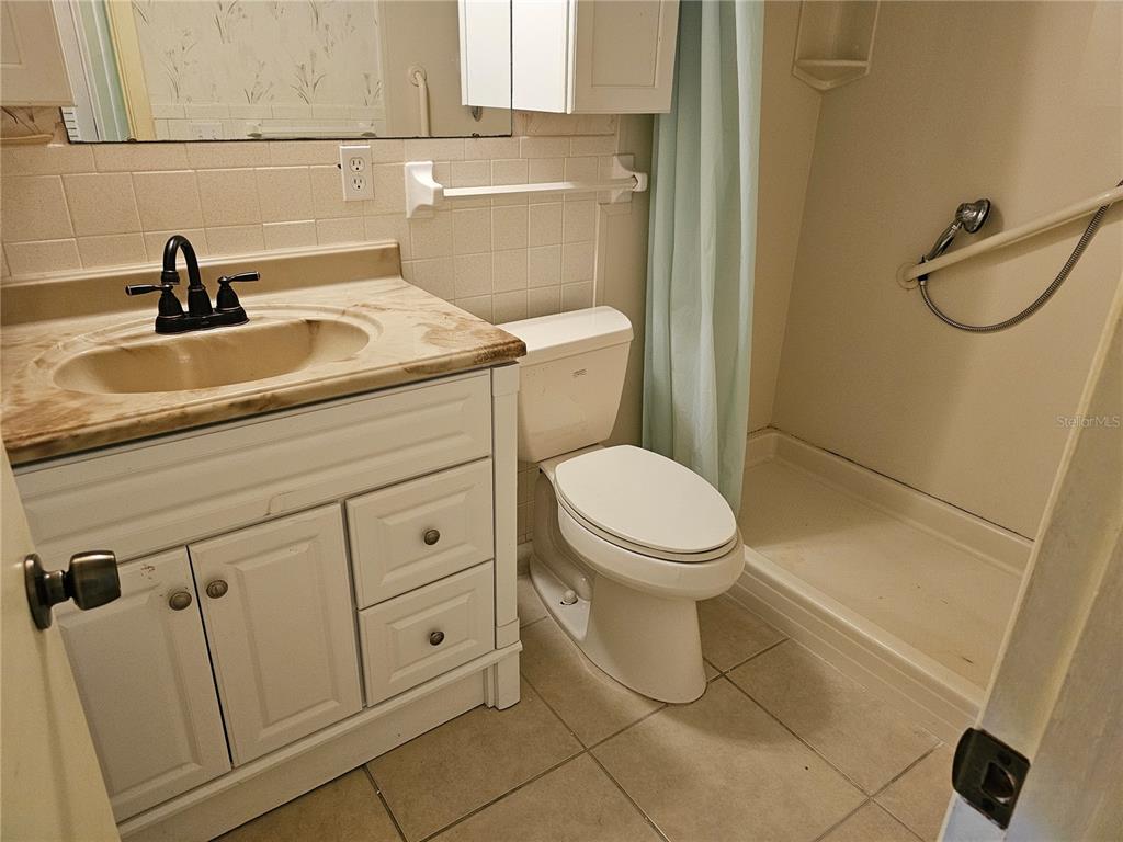 A bathroom features a white vanity, a toilet, and a walk-in shower with a curtain — 4747 AZALEA DRIVE UNIT 125, NEW PORT RICHEY, FL