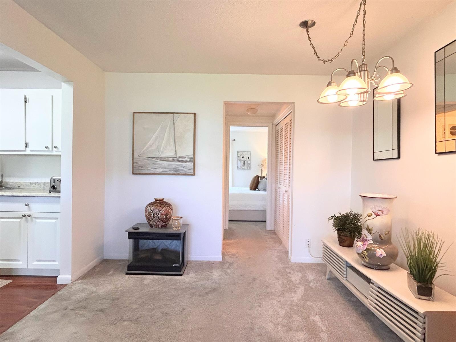 A carpeted living area features a small fireplace, a chandelier, and a view into a bedroom — 320 Horizons # 103, Boynton Beach FL 33435, BOYNTON BEACH, FL