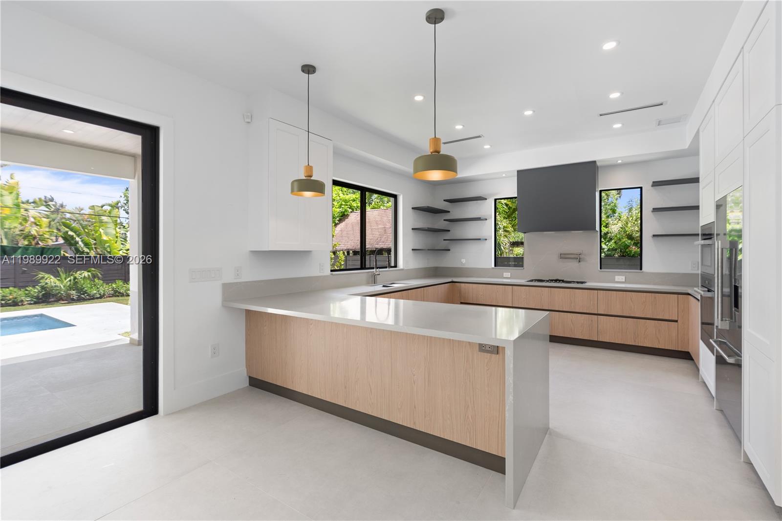 A modern kitchen features light wood cabinets, white countertops, floating shelves, and a backyard view — 6221 SW 60th St, South Miami FL 33143, SOUTH MIAMI, FL