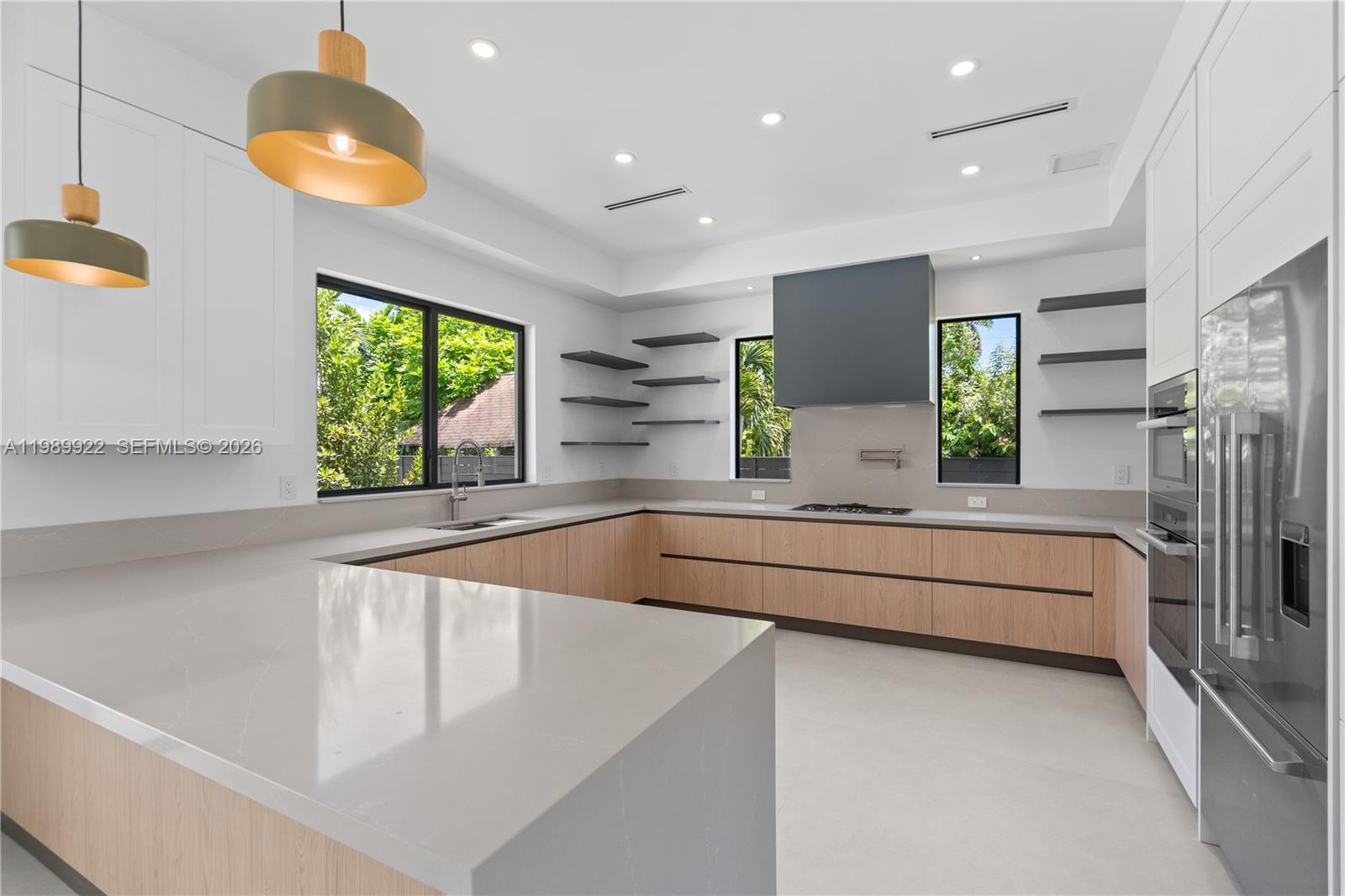A modern kitchen features light wood cabinetry, white countertops, floating shelves, and stainless steel appliances — 6221 SW 60th St, South Miami FL 33143, SOUTH MIAMI, FL