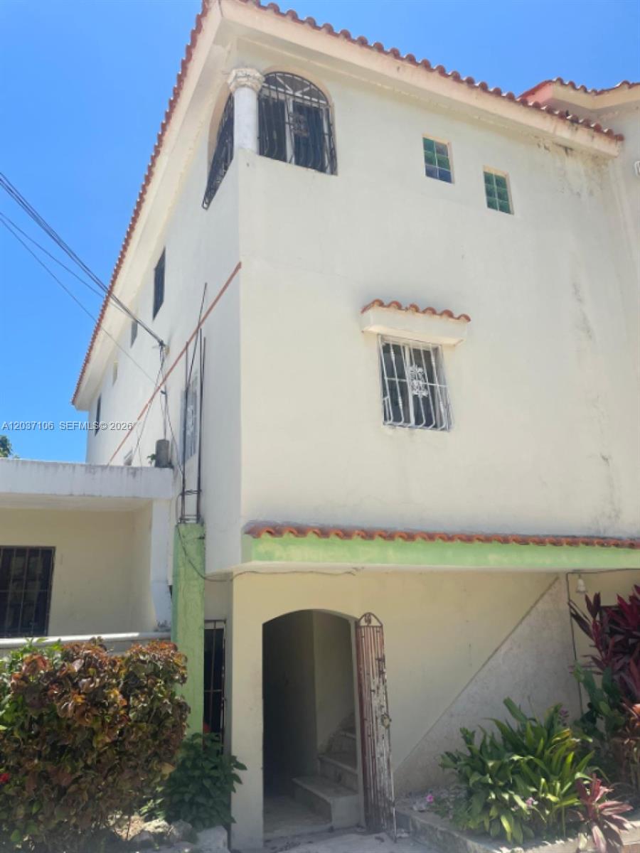 A multi-story stucco building features a tiled roof, arched entryway, and metal security bars — 0 Bàvarro # 0, FL