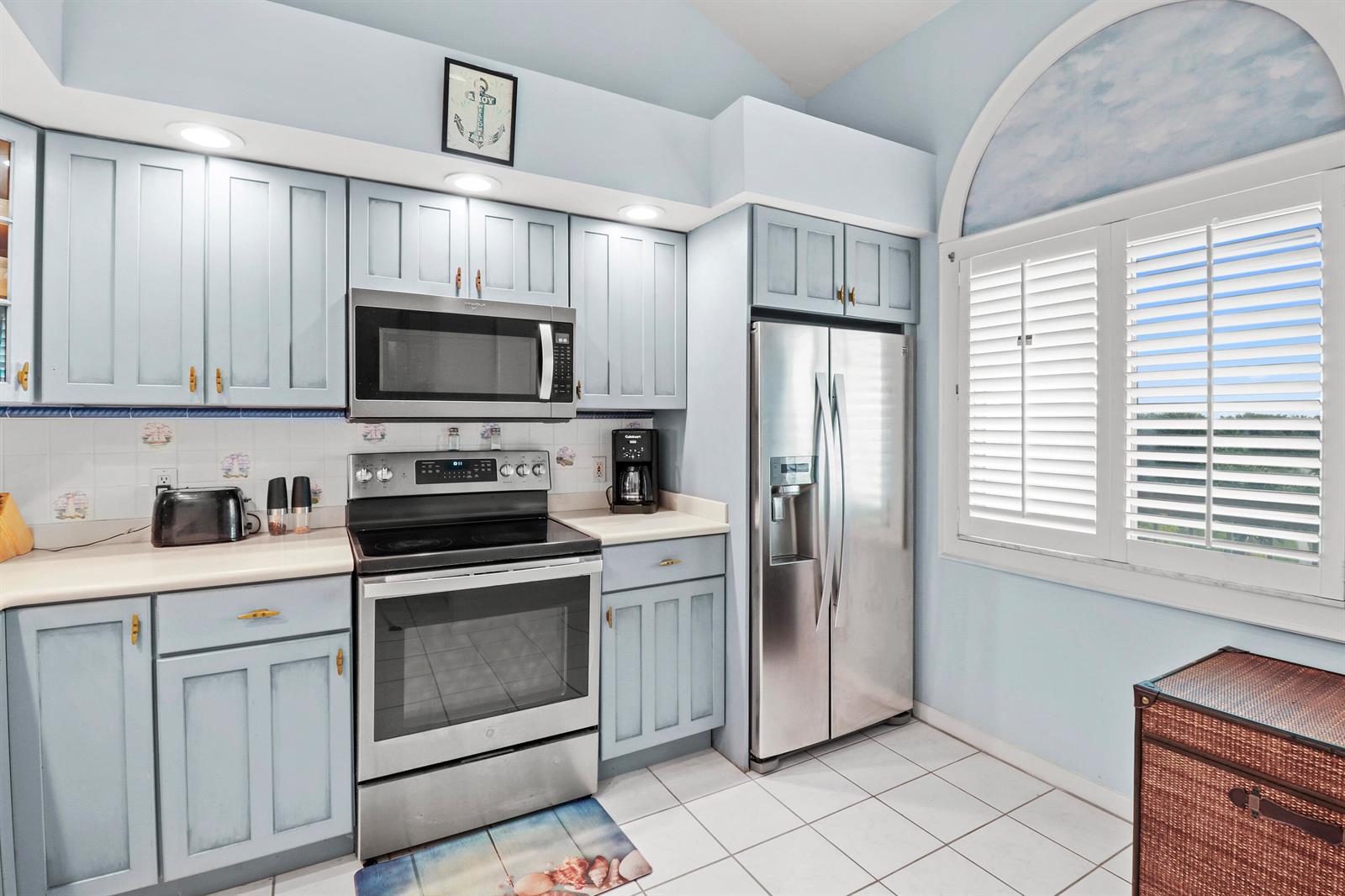 A kitchen features light blue cabinets, stainless steel appliances, white tile floors, and arched windows — 901 Seafarer Circle # 503, Jupiter FL 33477, JUPITER, FL