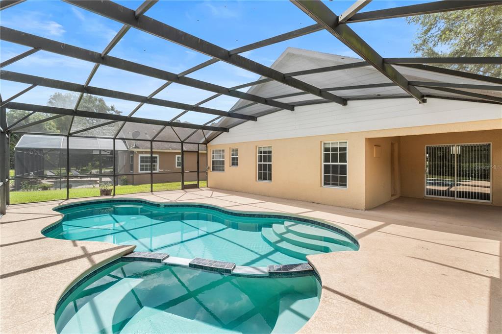 A screened-in patio features a swimming pool with an attached spa and concrete decking — 10990 ELIOTTI STREET, ORLANDO, FL