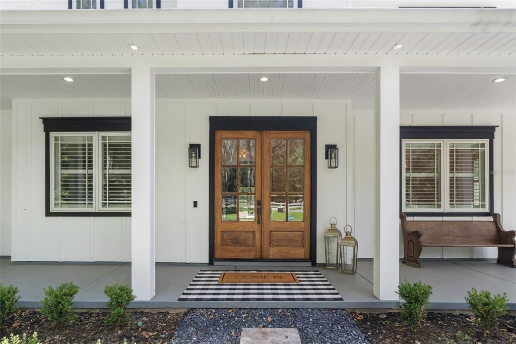 A covered front porch features white board-and-batten siding, double wood doors, and a black-and-white rug — 994 SW 37TH PLACE ROAD, OCALA, FL