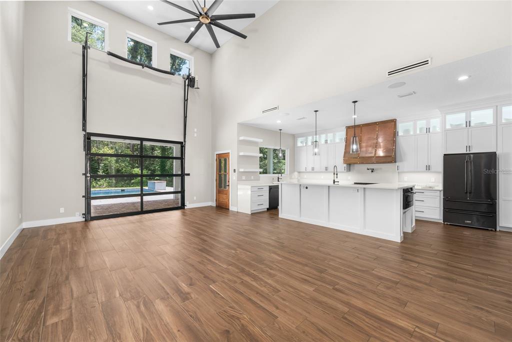 A spacious open-concept kitchen and living area features wood-look flooring and a large glass garage-style door — 994 SW 37TH PLACE ROAD, OCALA, FL