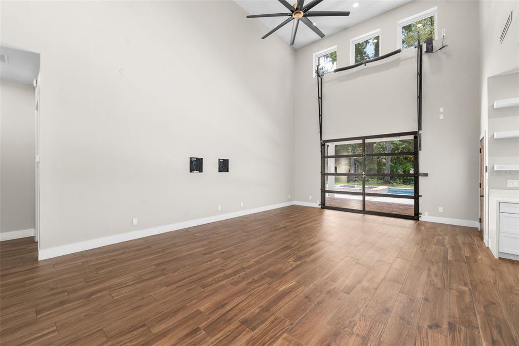 A spacious living room features wood-look tile floors, high ceilings, and a large glass garage door — 994 SW 37TH PLACE ROAD, OCALA, FL