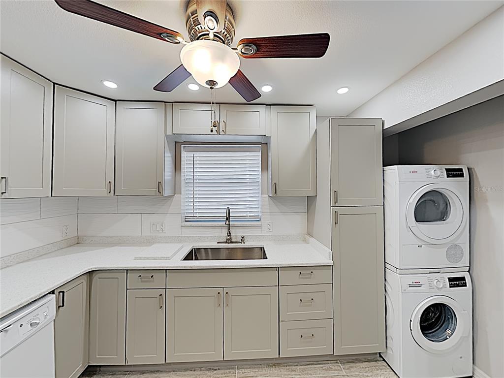 A laundry room features light gray cabinets, white countertops, a stainless steel sink, and stacked appliances — 525 CONWAY ROAD UNIT 91, ORLANDO, FL