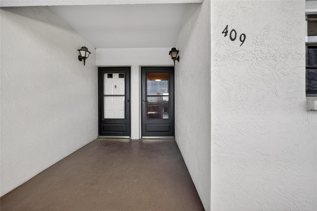 A covered entryway features two black doors, two wall-mounted lanterns, and the number 409 — 6080 80TH STREET N UNIT 409, ST PETERSBURG, FL