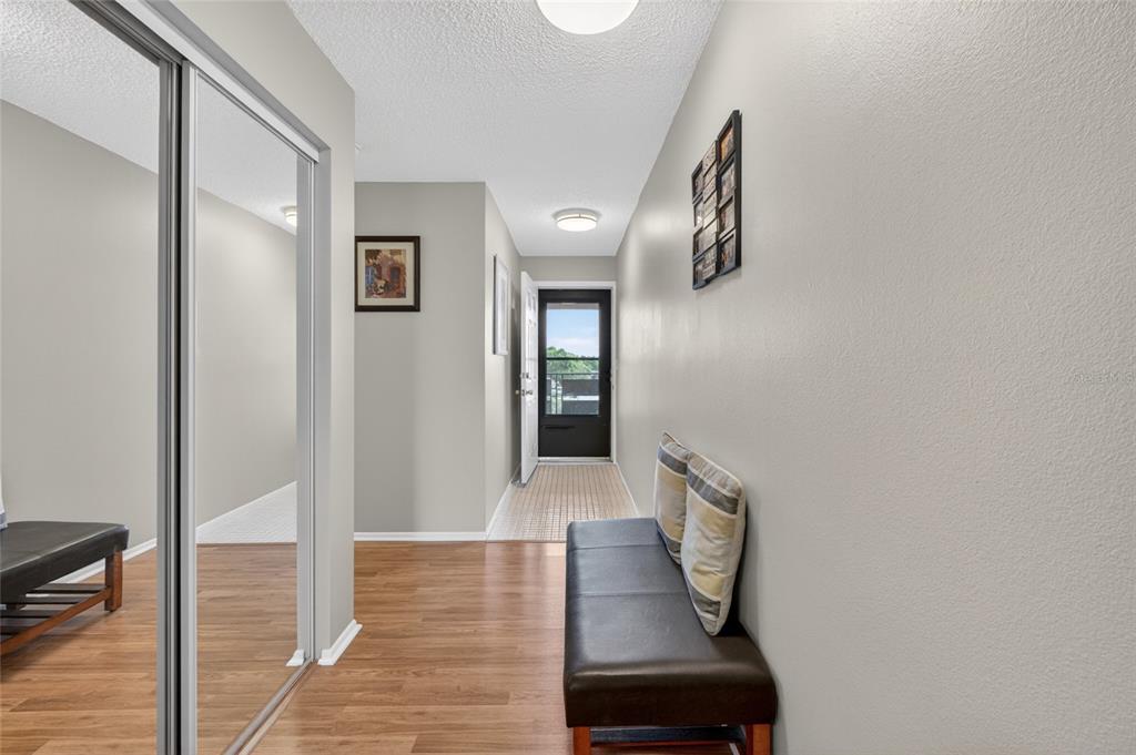 A hallway with wood-look flooring, a mirrored closet, a bench, and a glass-paneled exterior door — 6080 80TH STREET N UNIT 409, ST PETERSBURG, FL