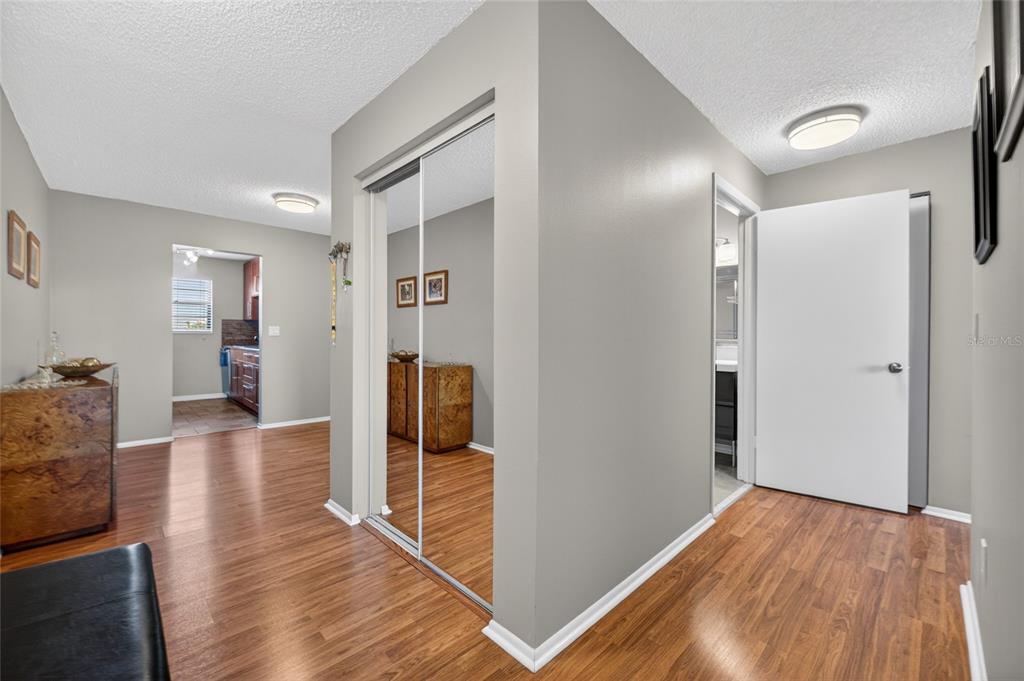 A hallway with wood-look flooring, mirrored closet doors, and a doorway leading to a kitchen — 6080 80TH STREET N UNIT 409, ST PETERSBURG, FL