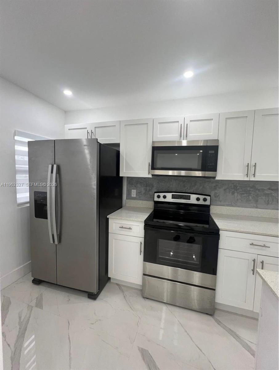 A kitchen features white cabinets, stainless steel appliances, and light-colored marble-patterned tile flooring — 1015 S 17th Ave # 10, Hollywood FL 33020, HOLLYWOOD, FL