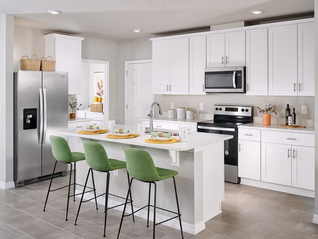 A modern kitchen features white cabinets, stainless steel appliances, a center island, and green stools — 646 PENNYWORT STREET, LAKE ALFRED, FL