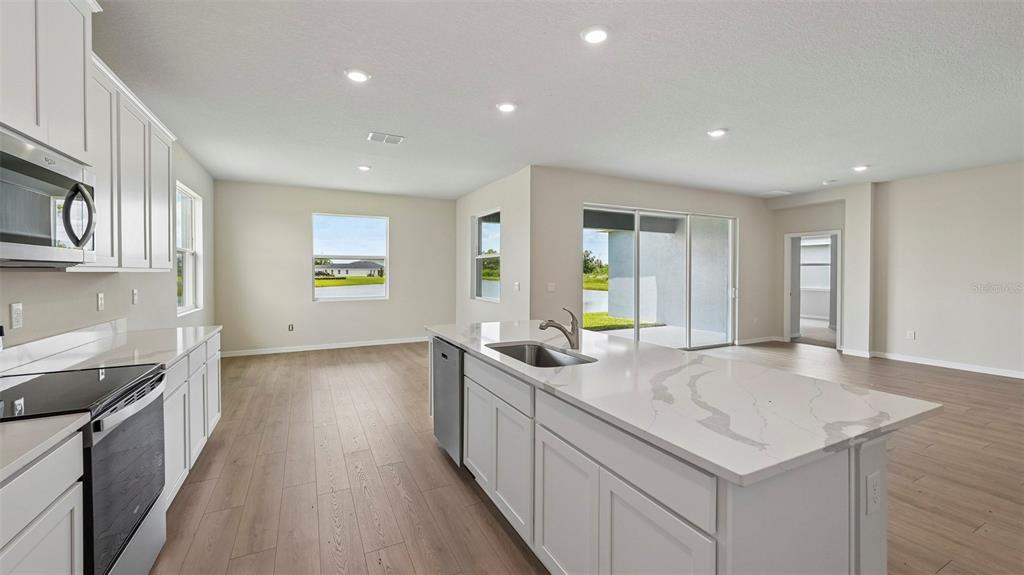 A modern kitchen features white cabinets, quartz countertops, a center island, and light wood flooring — 10429 WOODLAND GARDEN WAY, PARRISH, FL
