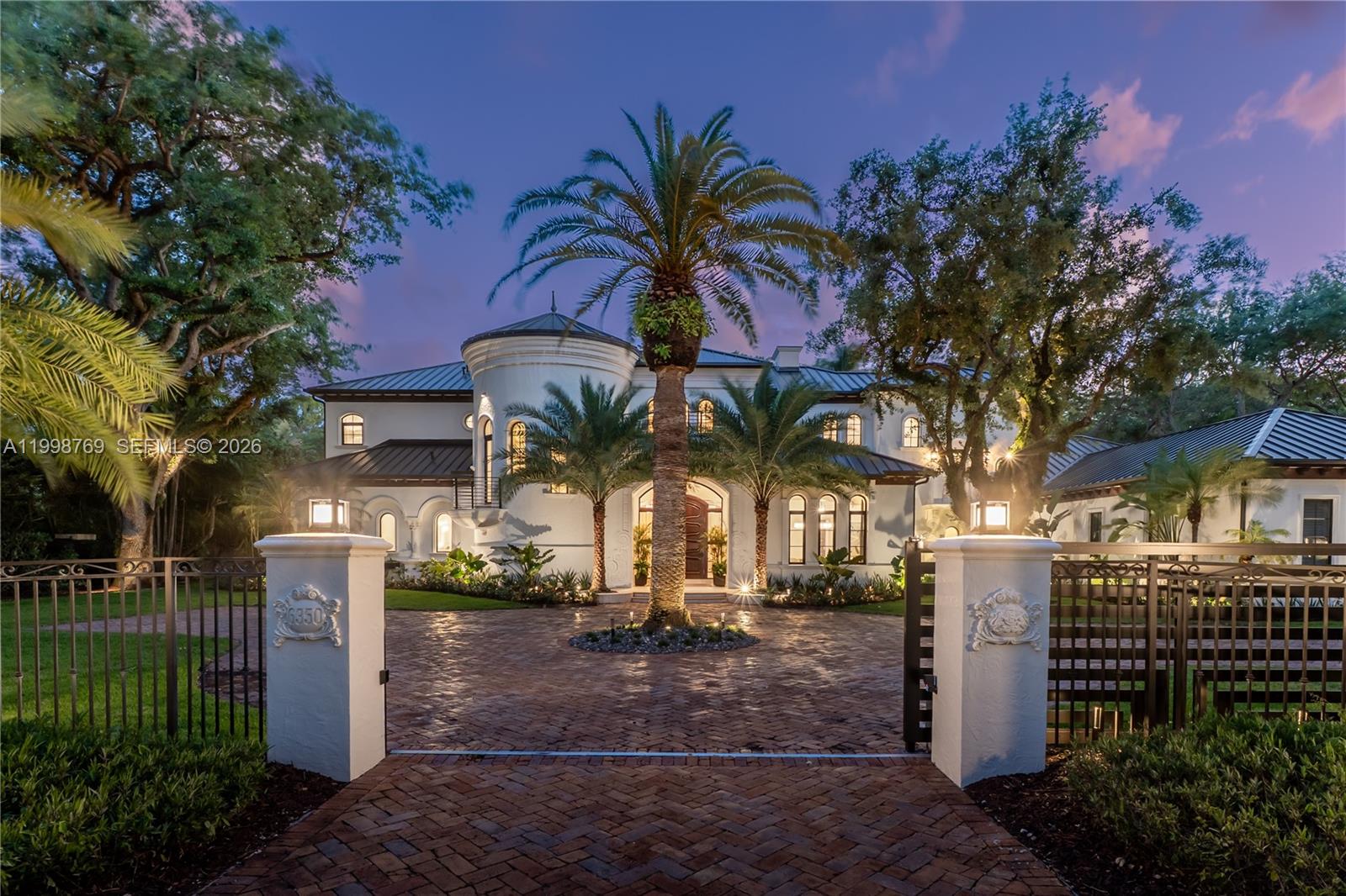 A large white two-story mansion with a circular tower and palm trees at dusk — 6350 SW 107th St, Pinecrest FL 33156, PINECREST, FL