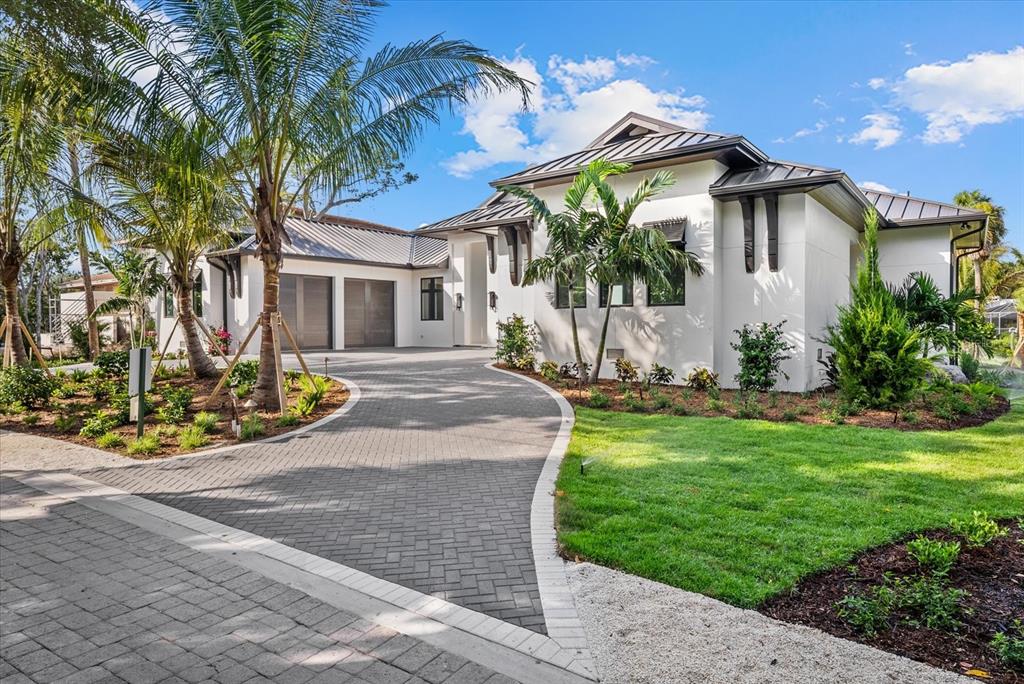 A modern white house features a dark metal roof, a curved paver driveway, and palm trees — 5215 HIDDEN HARBOR ROAD, SARASOTA, FL
