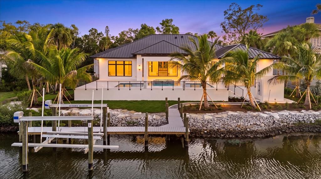 A waterfront house with a metal roof, pool deck, and private boat lift at dusk — 5215 HIDDEN HARBOR ROAD, SARASOTA, FL