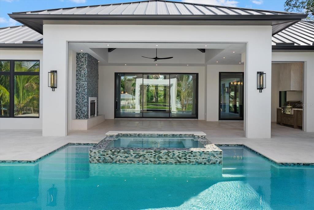 A modern covered patio features a tiled spa, swimming pool, fireplace, and large sliding doors — 5215 HIDDEN HARBOR ROAD, SARASOTA, FL