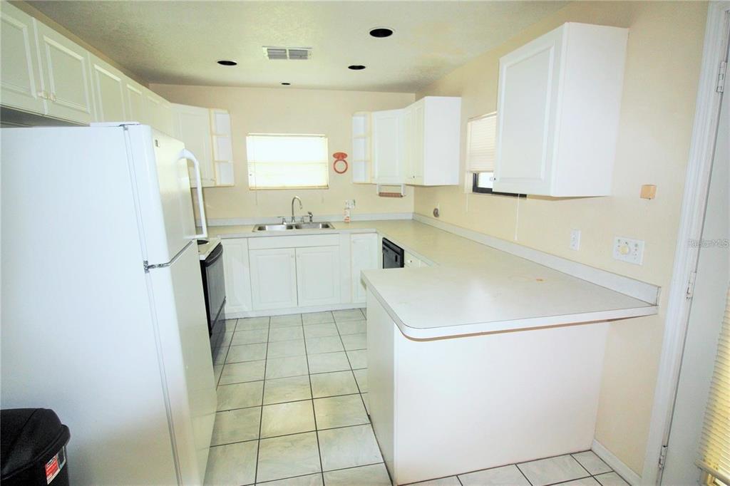 A kitchen features white cabinets, white appliances, a peninsula counter, and light-colored tile flooring — 521 20TH STREET SW UNIT C, WINTER HAVEN, FL