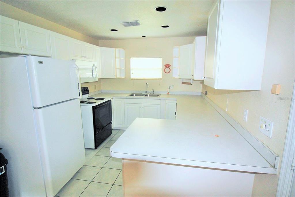 A kitchen features white cabinets, white appliances, a double sink, and light-colored tile flooring — 521 20TH STREET SW UNIT C, WINTER HAVEN, FL