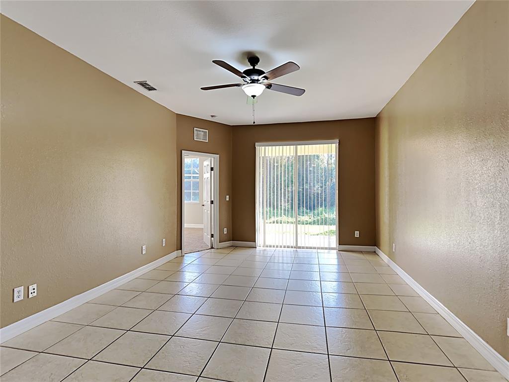 An empty room with tan walls, tile flooring, a ceiling fan, and sliding glass doors — 176 OCEAN BLUFF DRIVE, POINCIANA, FL
