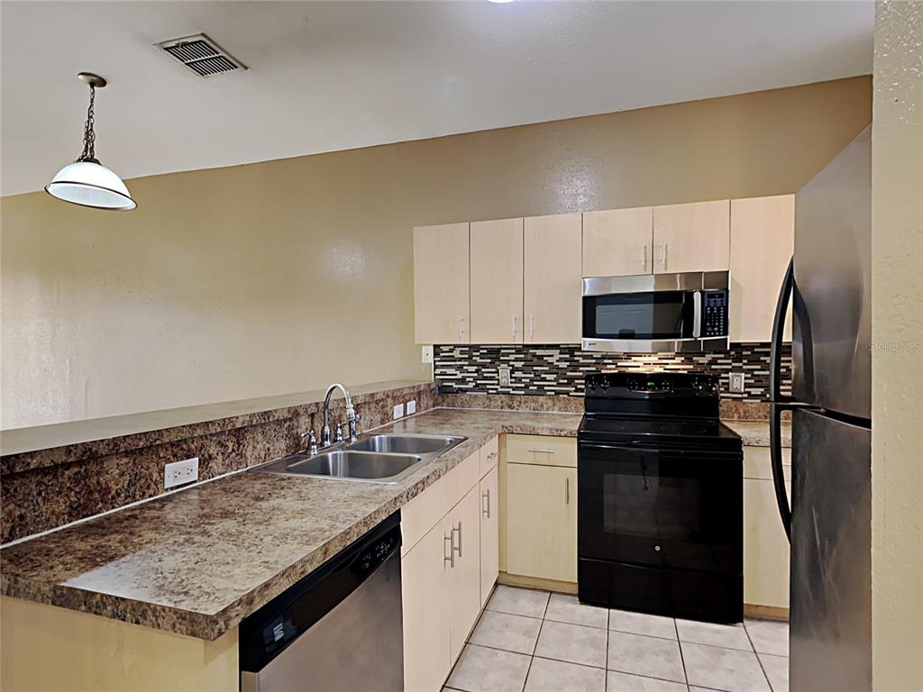A kitchen features light wood cabinets, dark granite countertops, stainless steel appliances, and tile flooring — 176 OCEAN BLUFF DRIVE, POINCIANA, FL