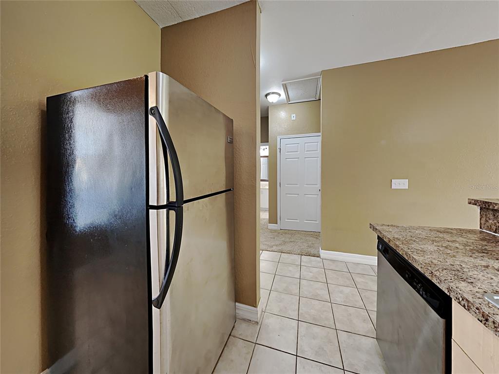 A kitchen features a stainless steel refrigerator, tile flooring, and a granite countertop — 176 OCEAN BLUFF DRIVE, POINCIANA, FL