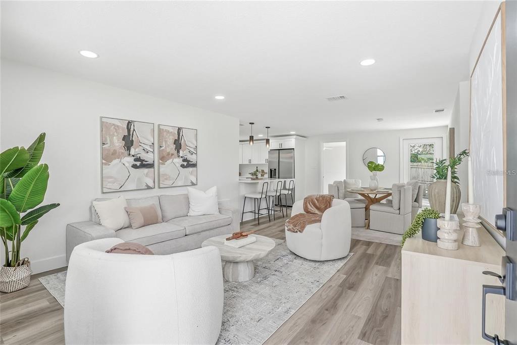 A modern, open-concept living and dining area features light wood flooring and neutral furnishings — 1004 IDLEBRIAR WAY, TARPON SPRINGS, FL