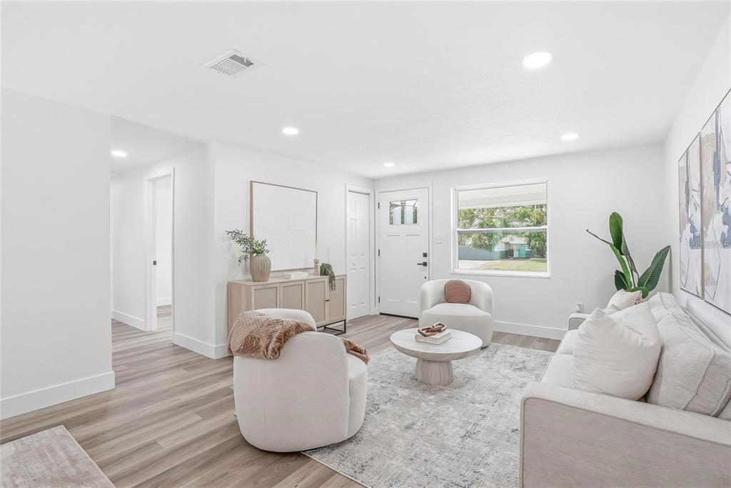 A bright living room features light wood-look flooring, white walls, two armchairs, and a sofa — 1004 IDLEBRIAR WAY, TARPON SPRINGS, FL